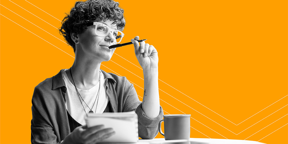 young woman with curly hair and glasses chewing on a pen while reading about handy tax tips for freelancers