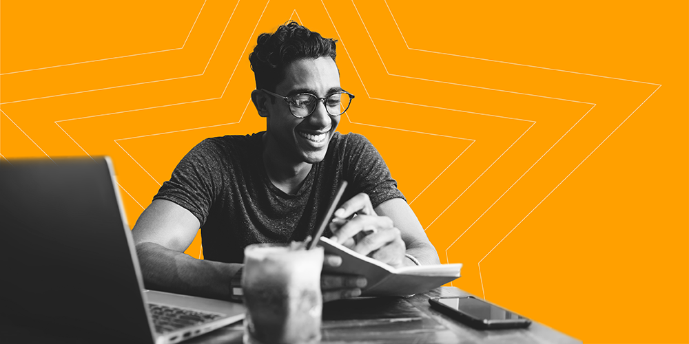 young man with glasses and an iced coffee looking at financial literacy books