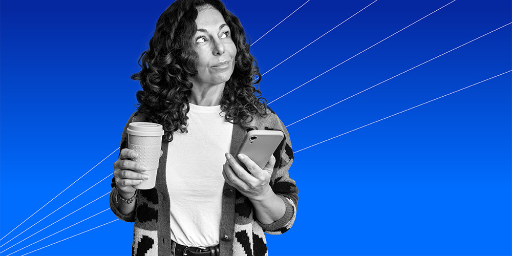 woman holding her coffee and cell phone and wondering is it worth keeping your landline?