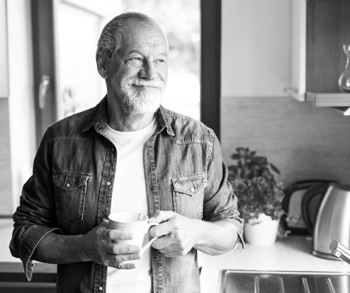 older man with a beard smiling and holding a coffee cup