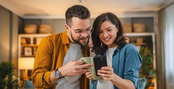 couple holding coffee cups and looking at smartphone