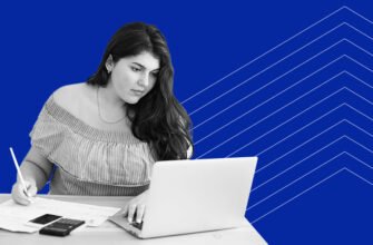 A woman sitting at a table with her laptop, pen and paper, and a calculator
