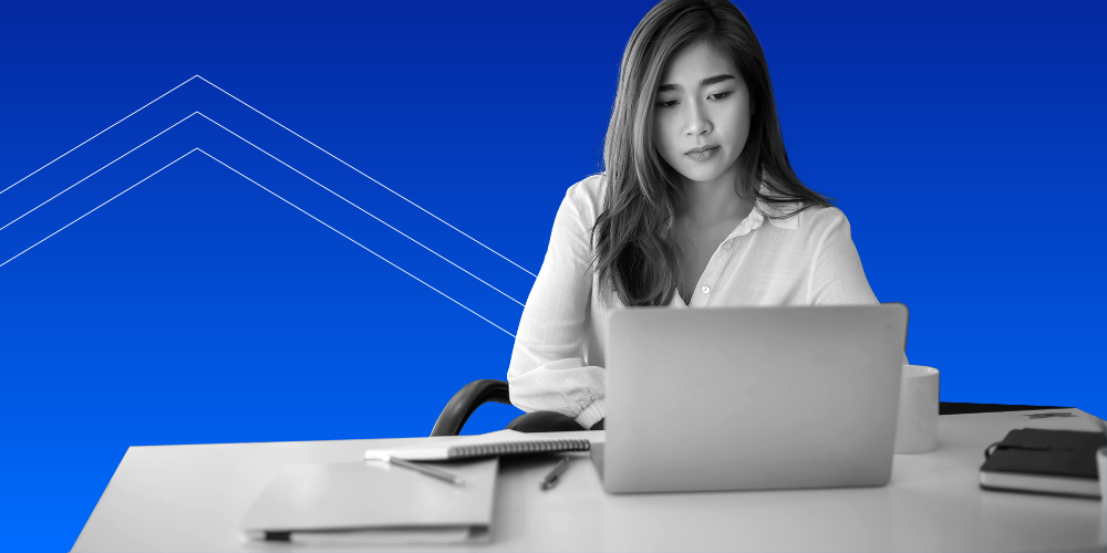 A woman looking at her laptop with a pad of paper next to her